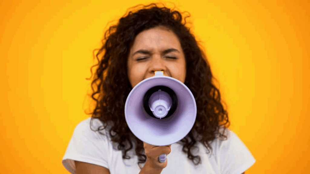 Photo d'une femme aux cheveux frisés criant dans un mégaphone sur un fond jaune vif, illustrant l'Initiative pour le renforcement de la gouvernance locale en matière de genre.