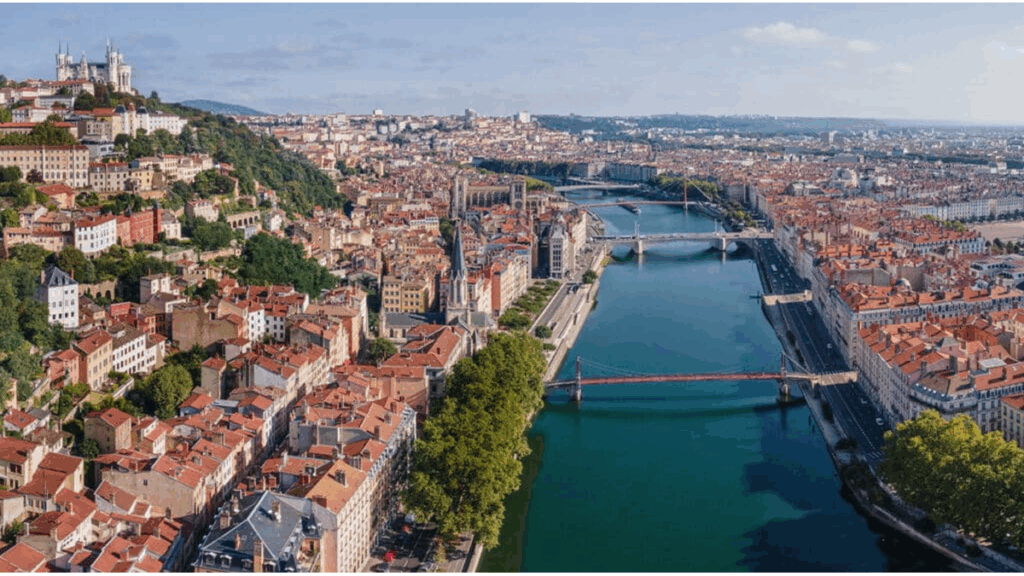 Vue aérienne panoramique de la ville de Lyon par temps ensoleillé, montrant les ponts sur la Saône et l'architecture dense du centre-ville historique.